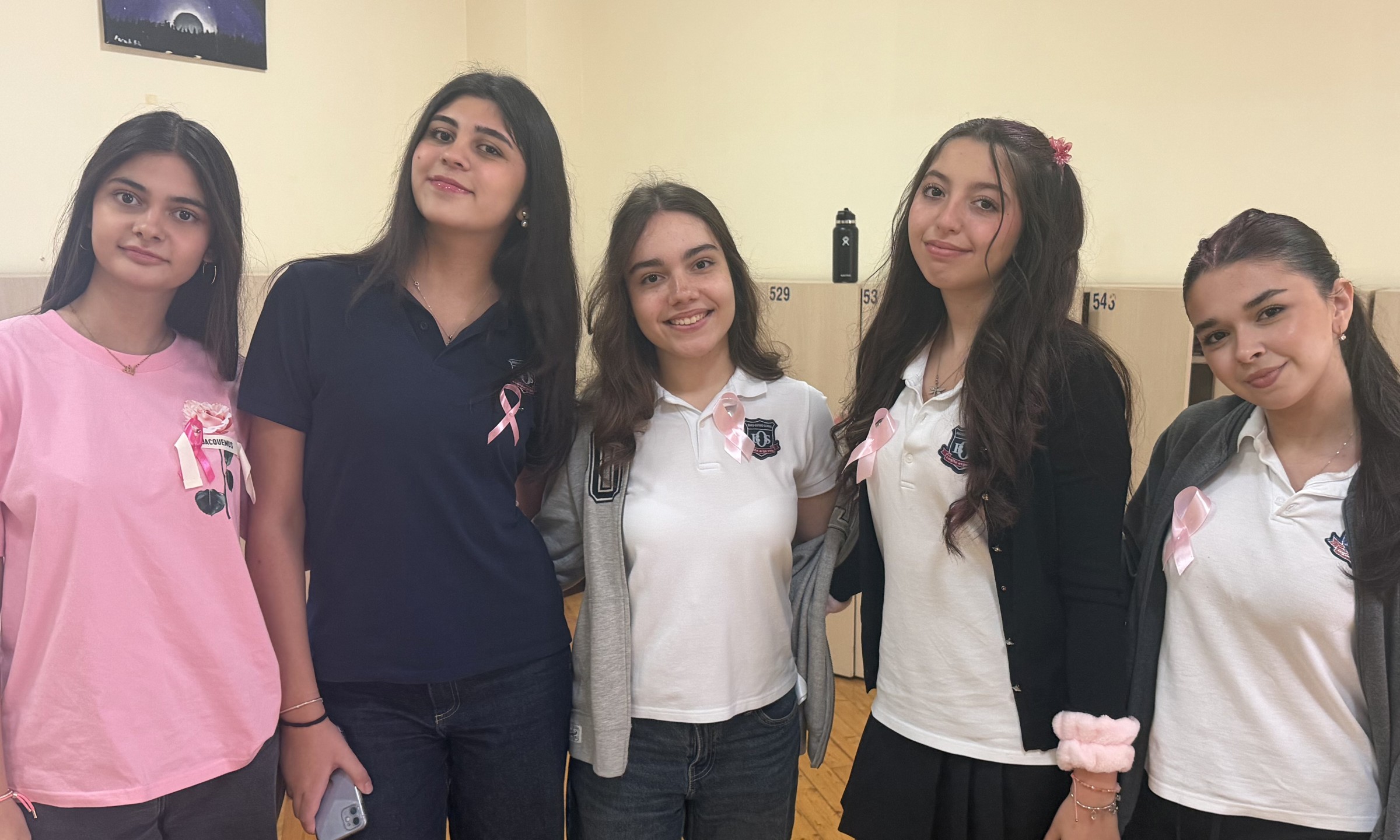 Five HERithm community members standing together wearing pink clothing and ribbons for Breast Cancer Awareness Month.